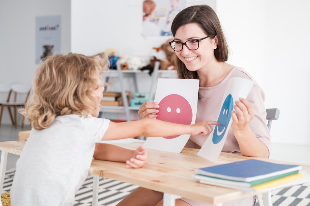 Smiling counselor holding pictures during meeting with young patient with autism