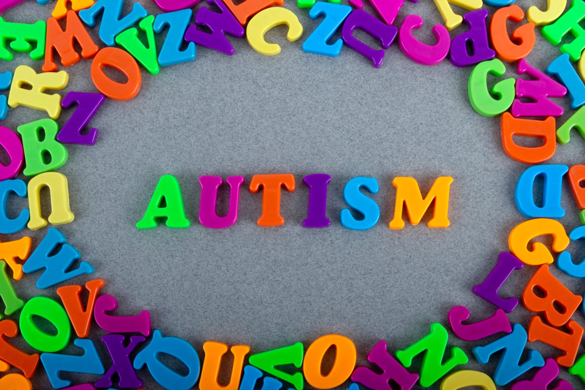 Multicolored letters and the word autism on a grey background. World Autism Awareness Day. Autism spectrum disorder concept.